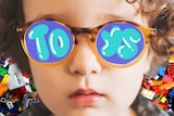 Child with sunglasses on that reflects the word toys, for a story about childhood toy addiction.