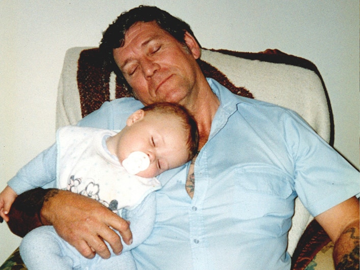 A man sits in a lounge chair holding a baby.