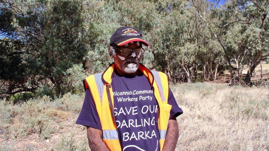 An Aboriginal man wears a save our darling baaka shirt. He is surrounded by trees