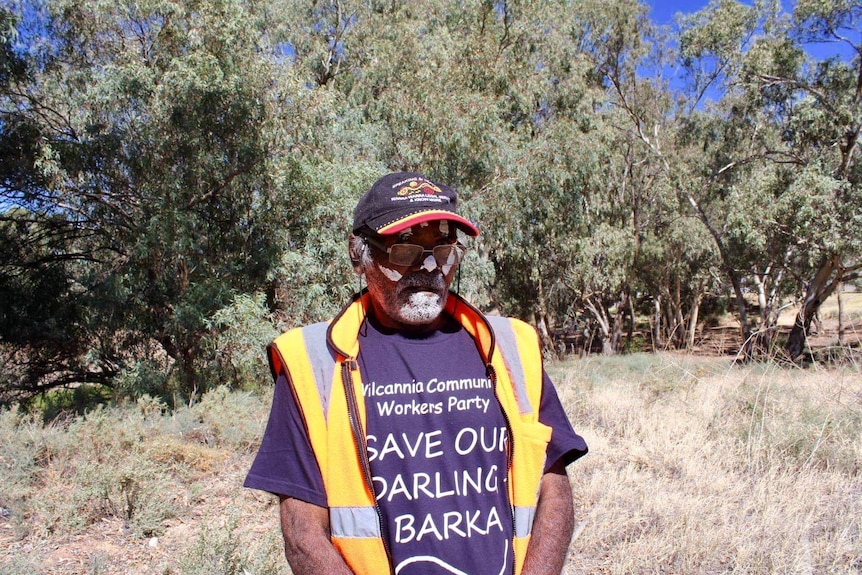 An Aboriginal man wears a save our darling baaka shirt. He is surrounded by trees