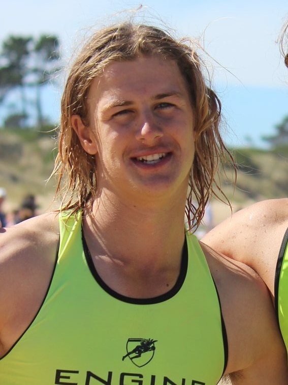 A young man with longish wet blonde hair in a lifesaving outfit.