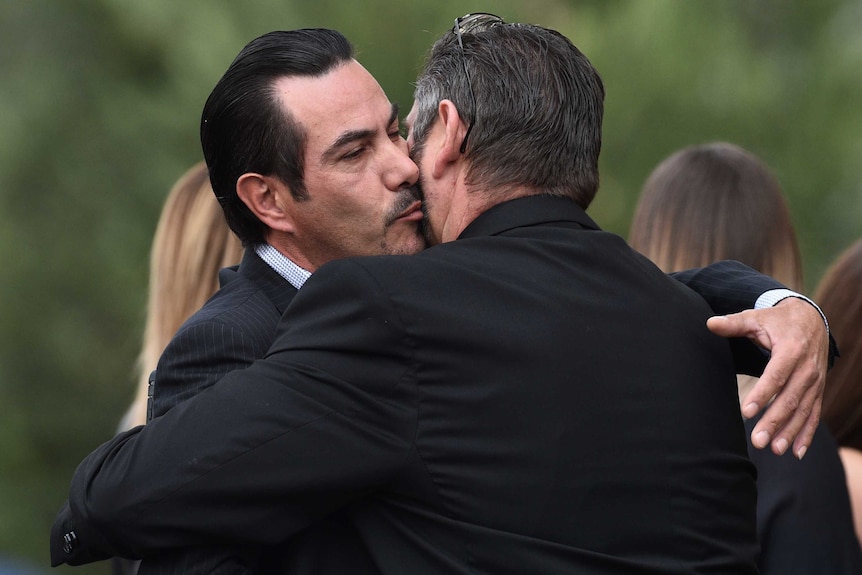 Two men wearing suits embrace.