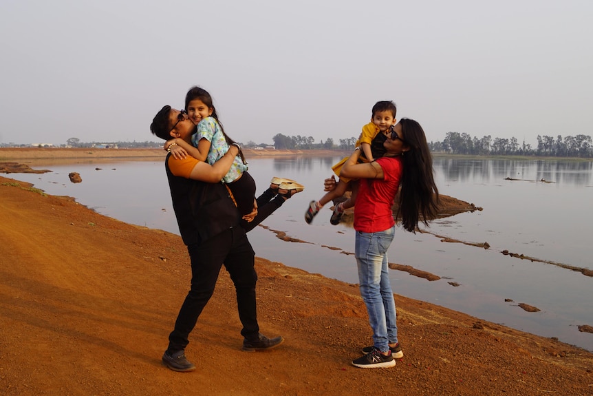 A couple holding kids in the air while standing next to a lake