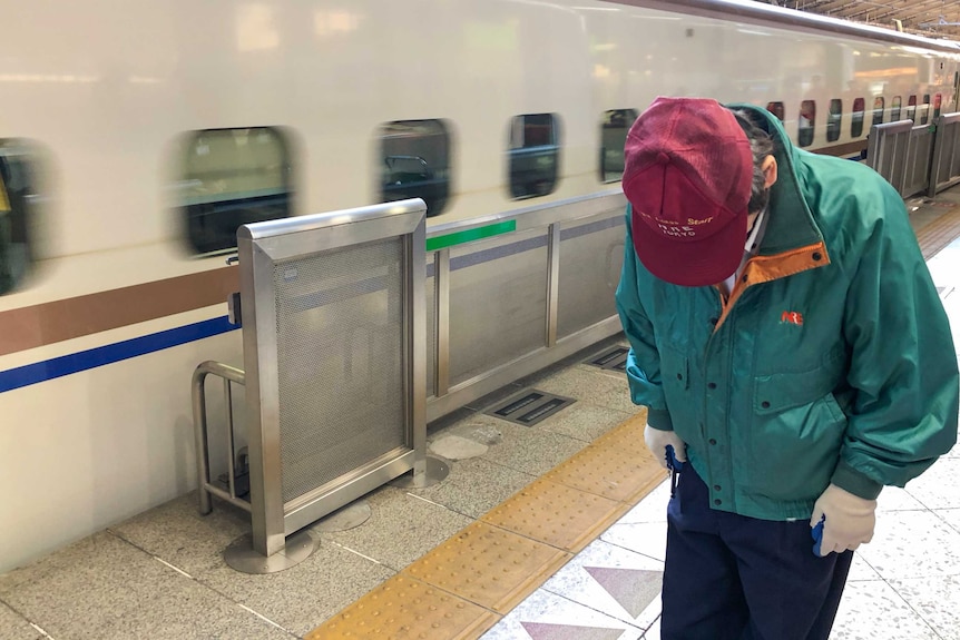 A Japan Rail worker bows as a shinkansen (bullet train) approaches