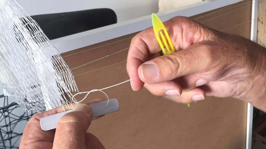 Man holding a meshing needle and board used for cast net making