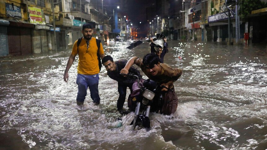 three boys push a motorbike through knee deep water in a city street