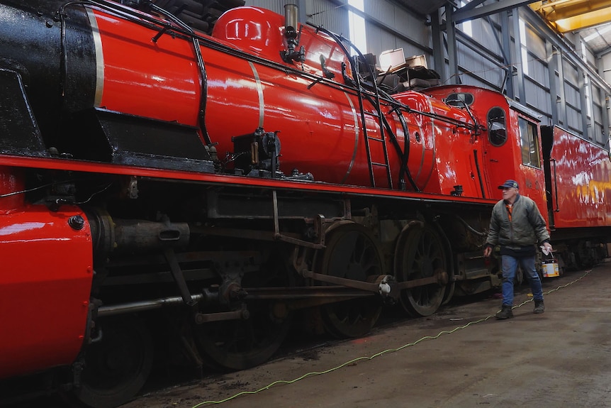 Elderly man with paint tin walking alongside huge red steam engine.
