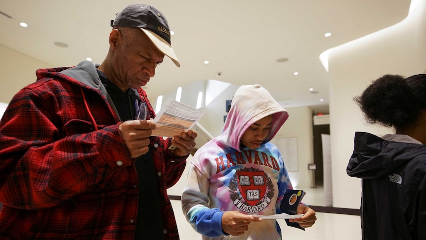 A man and woman, both wearing winter clothes, look down at the printed sheets they hold in their hands