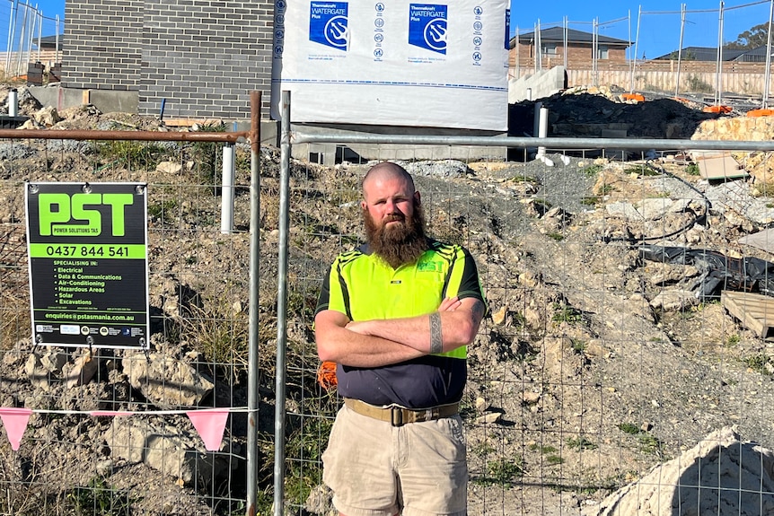 A man stands in front of a building site with his arms crossed