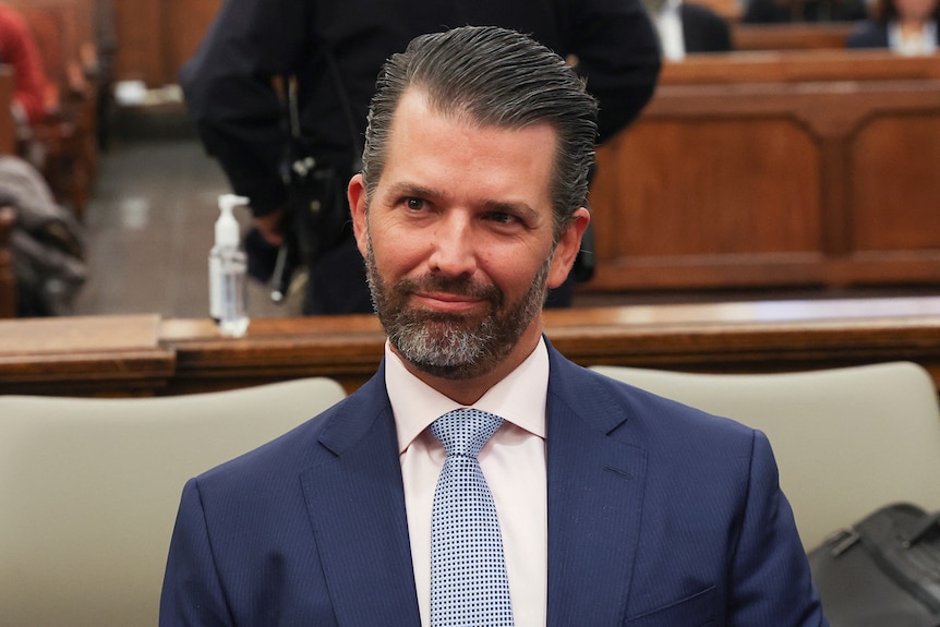 Donald Trump Jr portrait in court. He has short, black hair, wears a navy suit and is staring intensely, with a smirk.