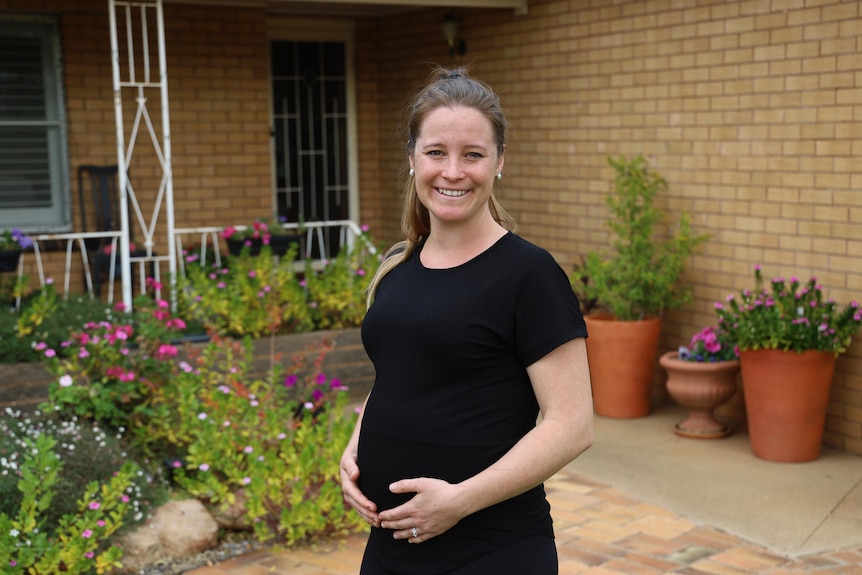 Woman holding her belly while pregnant, smiling for a photo