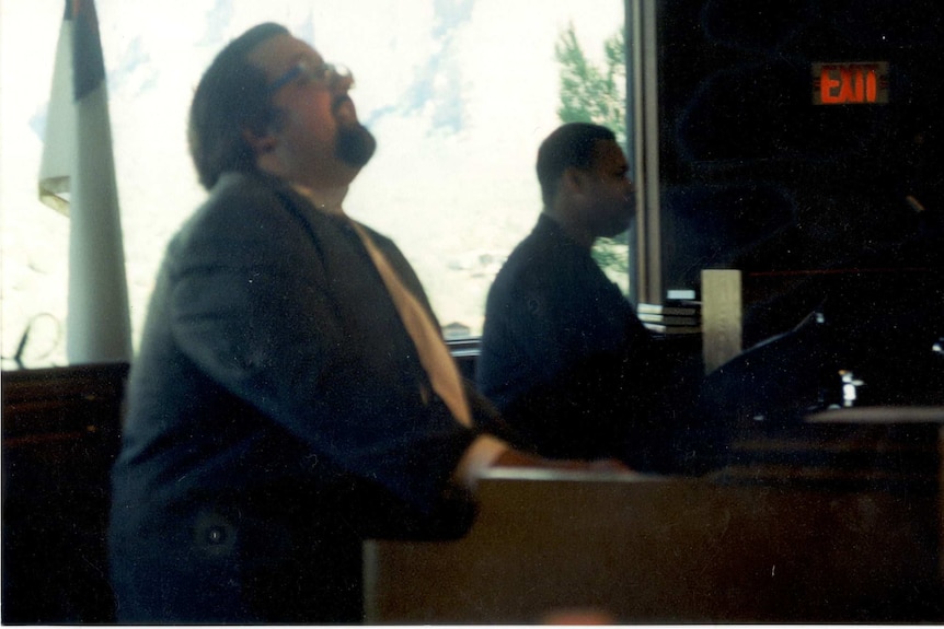 Two male musicians sit side by side; the man in the foreground plays an organ.