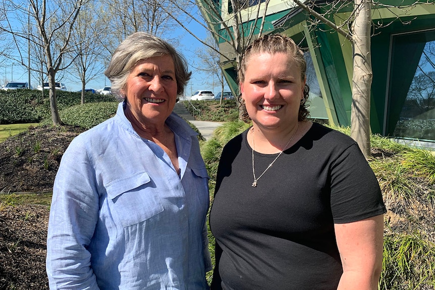 Two women stand side by side outdoors and look at the camera.