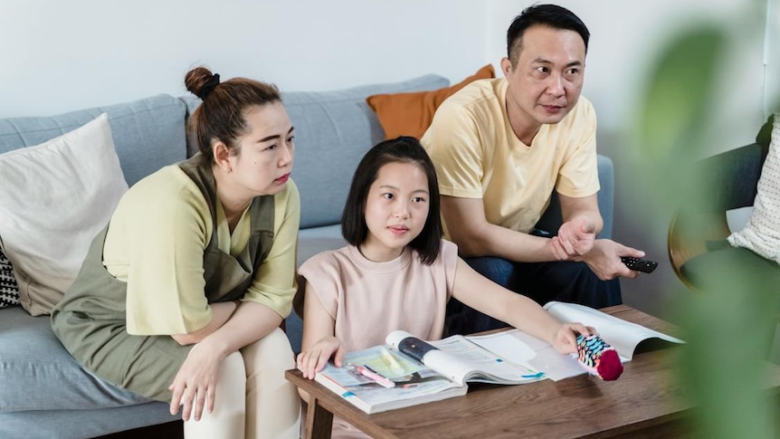 A woman and man sit on a couch with a younger woman sitting in the middle of them 