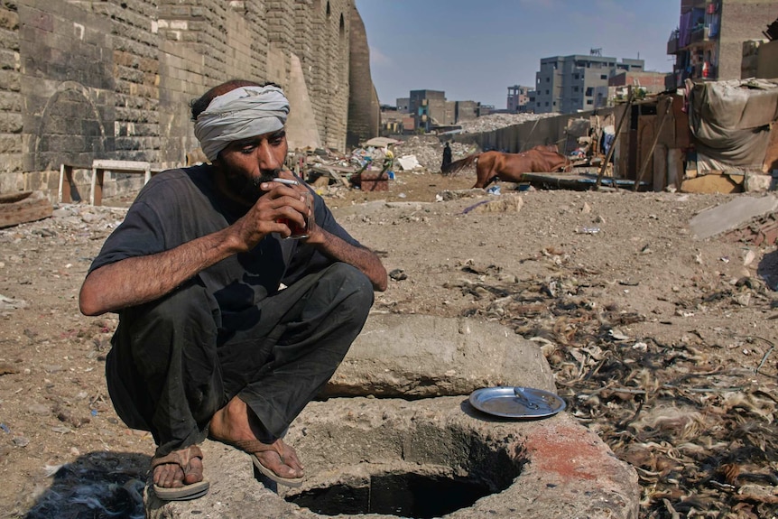 Mohamed, a donkey and horse barber squats while drinking tea and smoking a cigarette