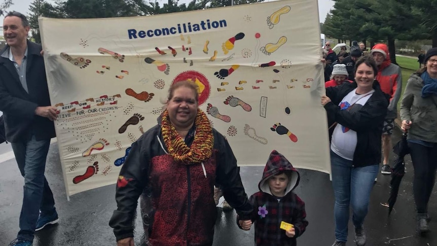 An Indigenous woman and boy walking in front of a banner.