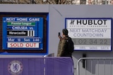 A Chelsea fan stands in front of a sign saying 'next home game Chelsea v Newcastle Mar 13 Sun 2.00 SOLD OUT".