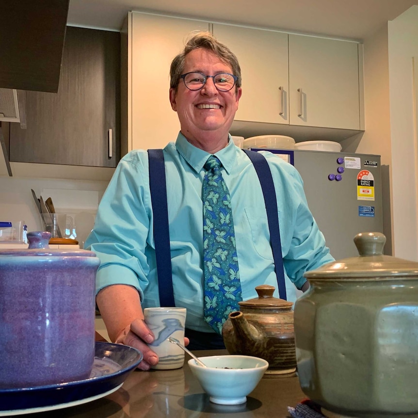 A man smiles with a cup of coffee.