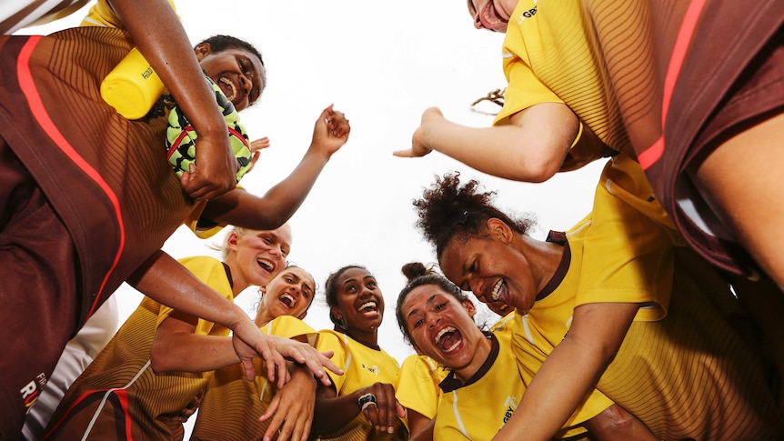 Members of the First Nations Women's Rugby Sevens squad smile and shout while in a huddle.