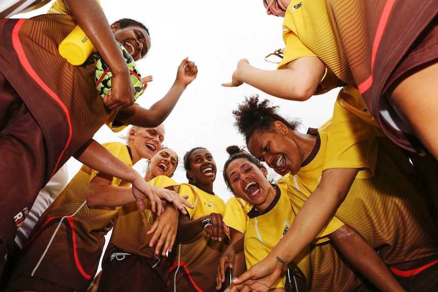 Members of the First Nations Women's Rugby Sevens squad smile and shout while in a huddle.