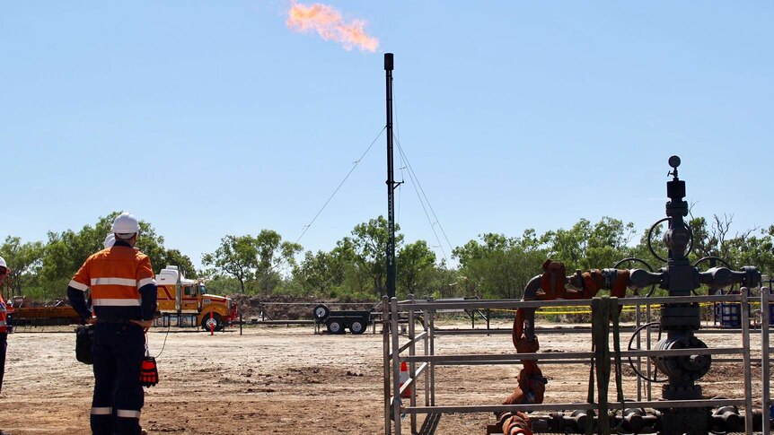 Origin employees stand near the Amungee shale gas wellhead with gas flaring in the background