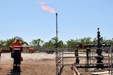 Origin employees stand near the Amungee shale gas wellhead with gas flaring in the background