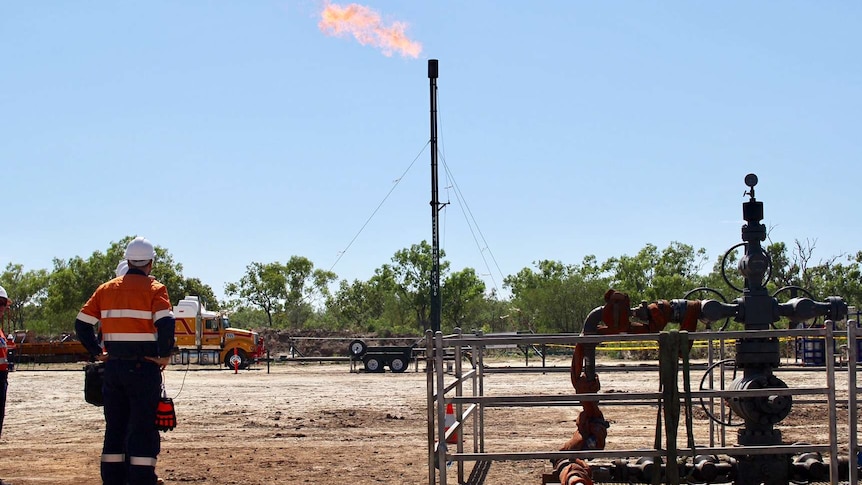 Origin employees stand near the Amungee shale gas wellhead with gas flaring in the background