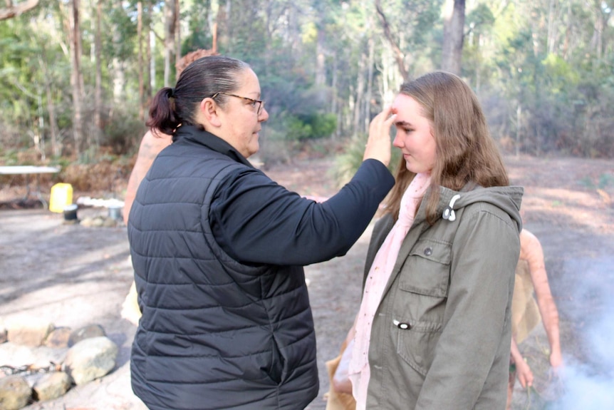 A woman paints younger woman's face with ochre.