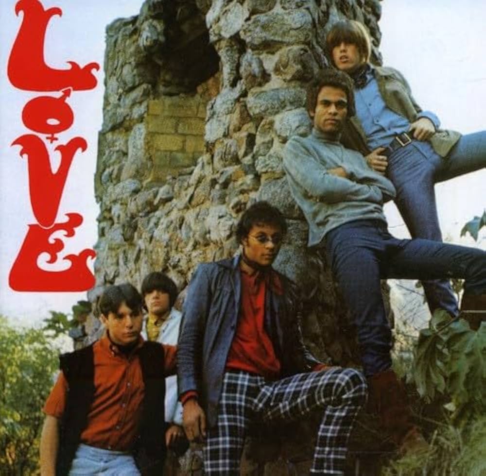 The band members stand outside near the remnants of a stone chimney.