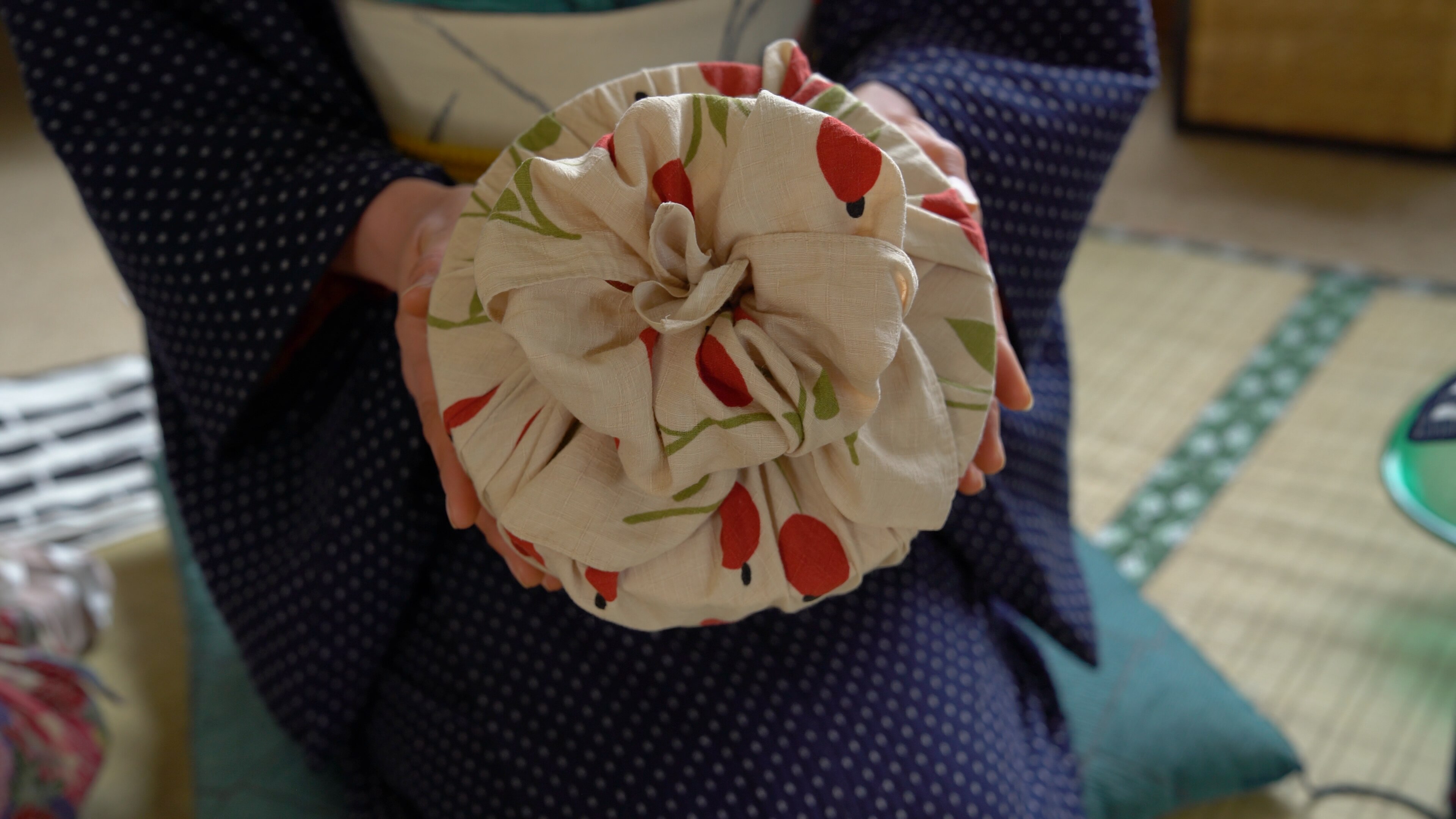 Yoko Nakawaza is holding a round gift in her hand wrapped in cream and red cotton fabric with a 'flower knot' on top.