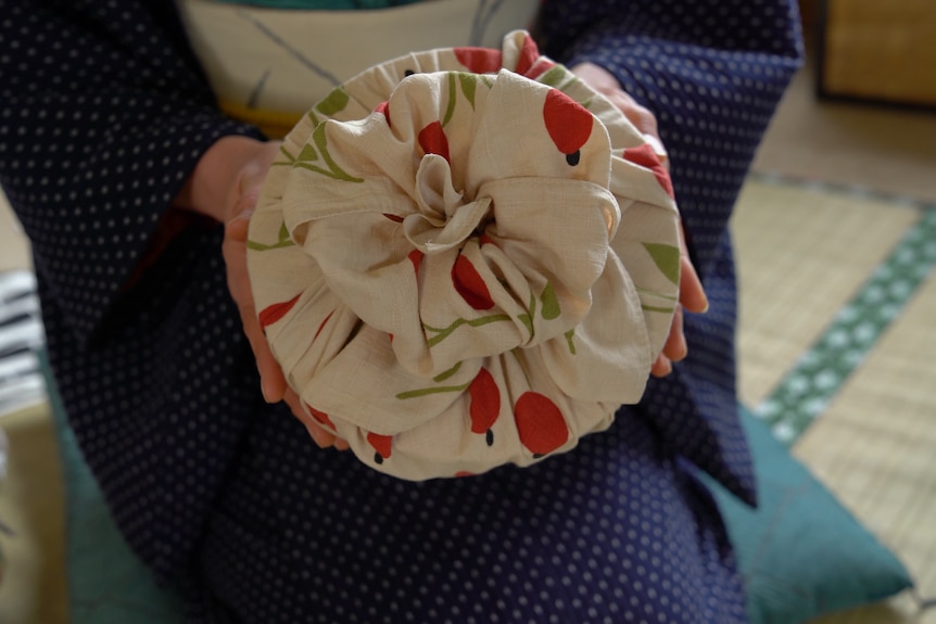 Yoko Nakawaza is holding a round gift in her hand wrapped in cream and red cotton fabric with a 'flower knot' on top.