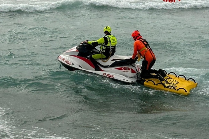 Two men in high-viz gear patrol choppy sea on jetski boat
