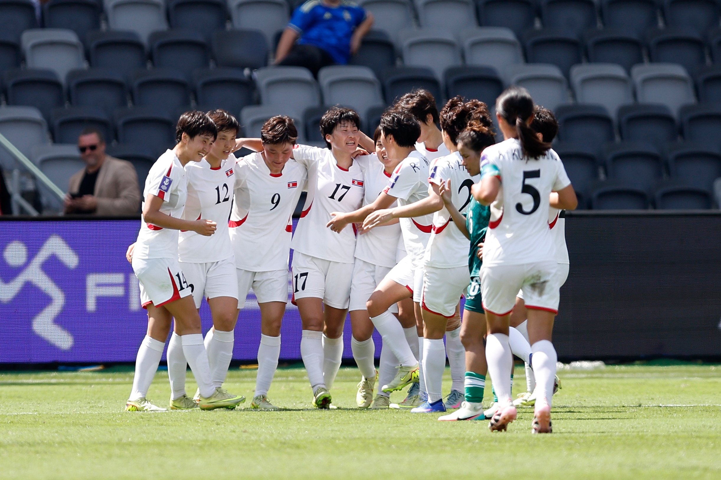 Um grupo de jogadores de futebol de branco se abraça e comemora ao sol