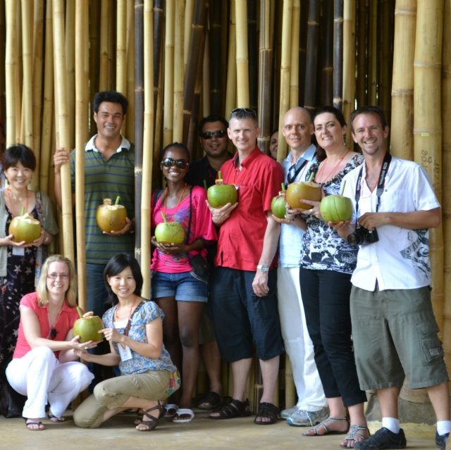 Karm wearing a red shirt standing with several friends all with coconut drinks in hand.