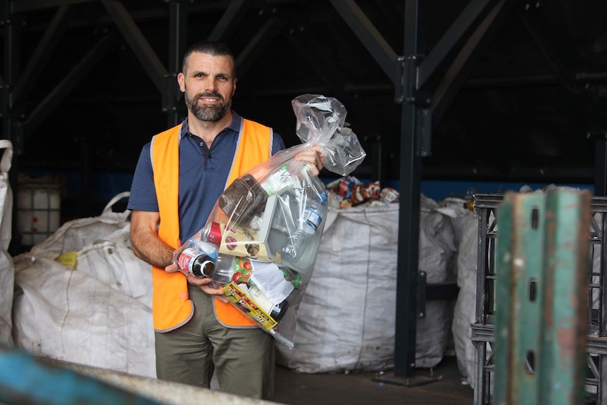 A photo of Dean Caton from NTRS smiling as he holds a bag of Glenys Goda's recyclable rubbish.