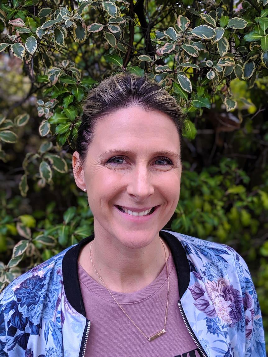 Danni Rowlands smiling at the camera in front of a green leafy bush.