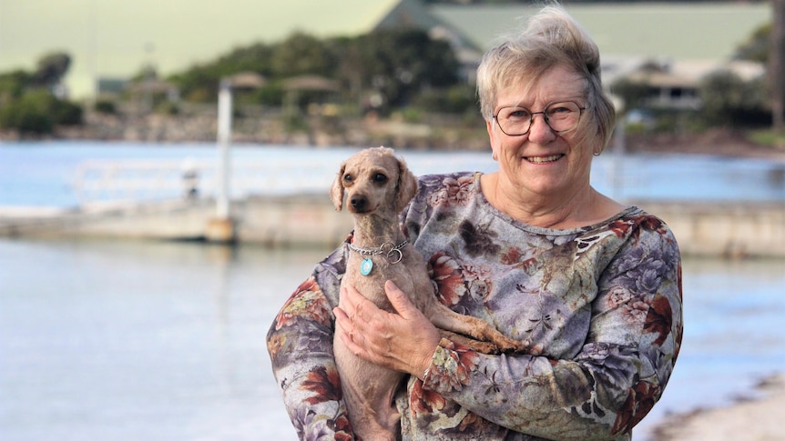 She stands in a floral top, holding a tiny dog, by the Esperance foreshore