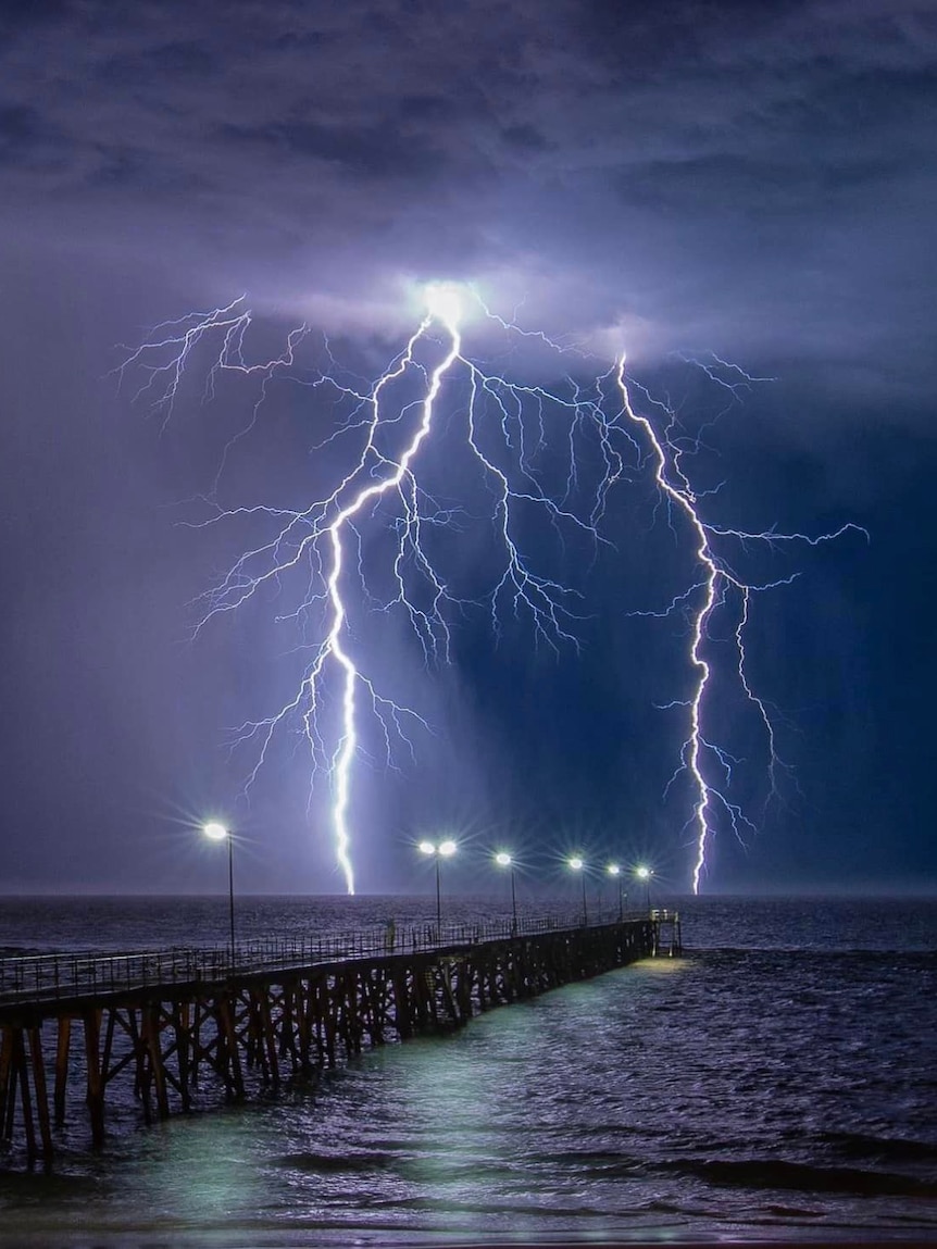 Lightning across a dark sky on a beach with a jetty