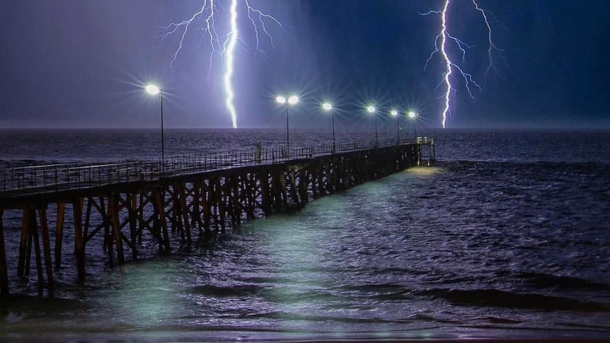 Lightning across a dark sky on a beach with a jetty