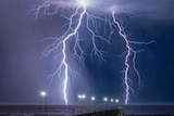 Lightning across a dark sky on a beach with a jetty