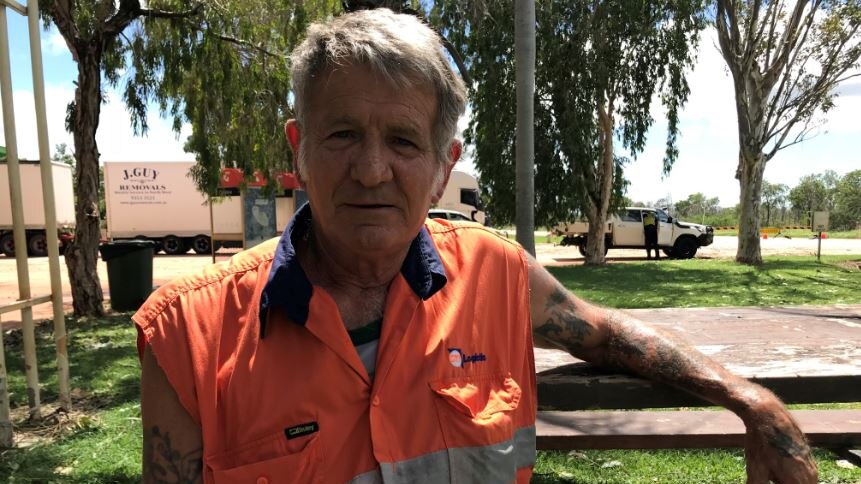 A man wearing an orange hi-vis work shirt sitting on a bench.