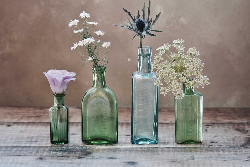 Four green glass bottles containing different flowers