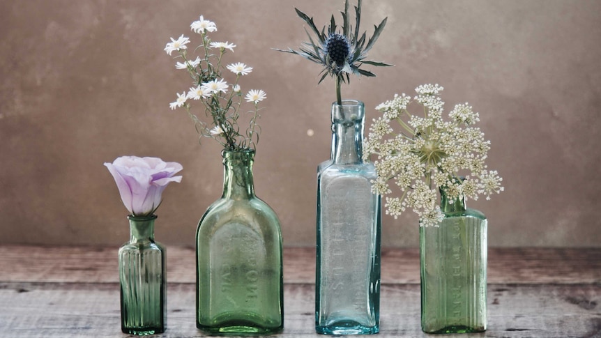 Four green glass bottles containing different flowers
