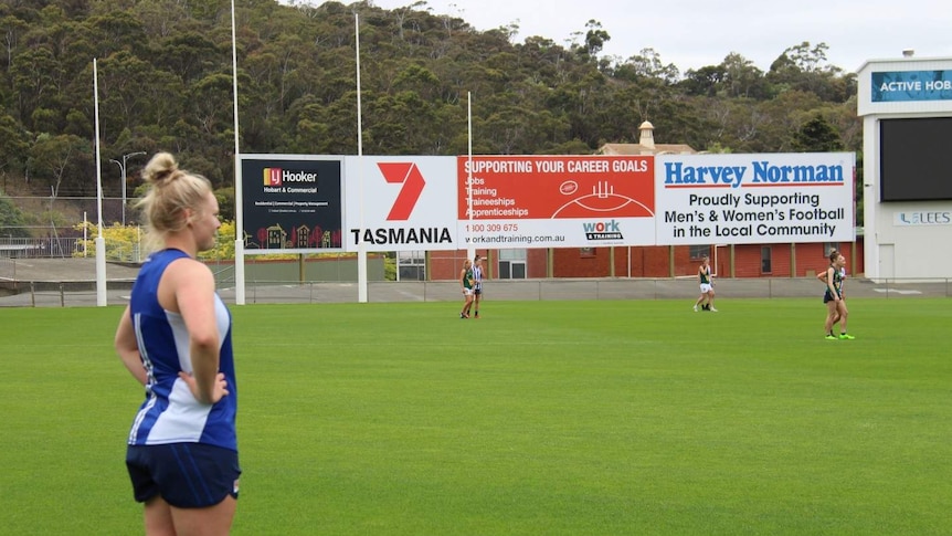 North Melbourne Tasmanian Kangaroos player Daria Bannister watches training from the side of a footy field