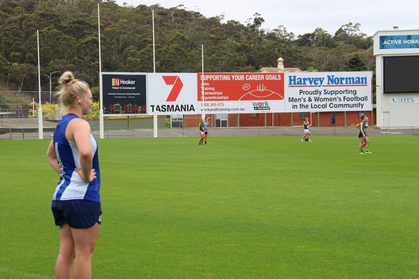 North Melbourne Tasmanian Kangaroos player Daria Bannister watches training from the side of a footy field