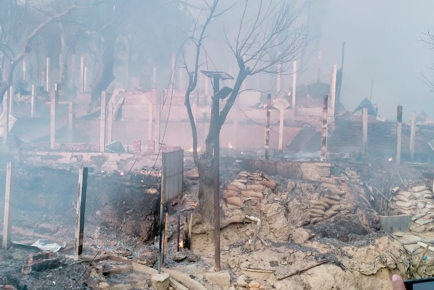 Une coquille brûlée d'un bâtiment et des arbres calcinés alors que la fumée monte du sol.