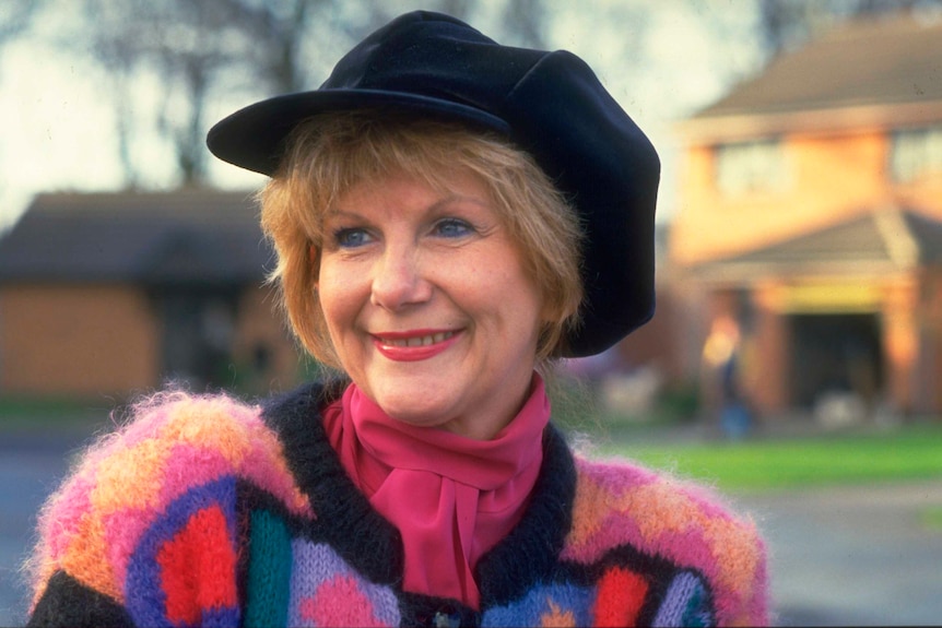 A woman smiling wearing a black hat and a brightly-coloured fluffy jumper.