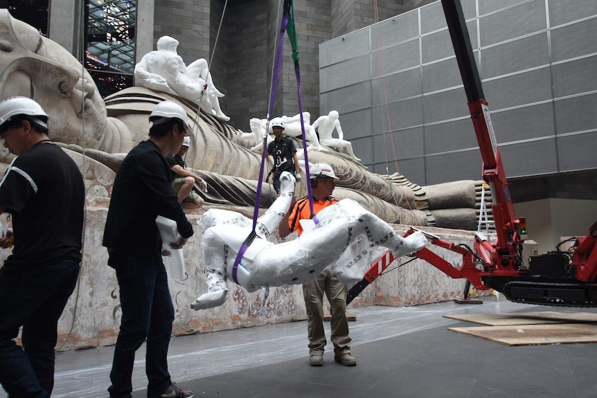 Workers attach a life-size sculpture onto a crane to be lifted into position.