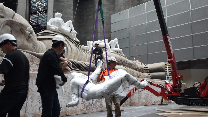 Workers attach a life-size sculpture onto a crane to be lifted into position.