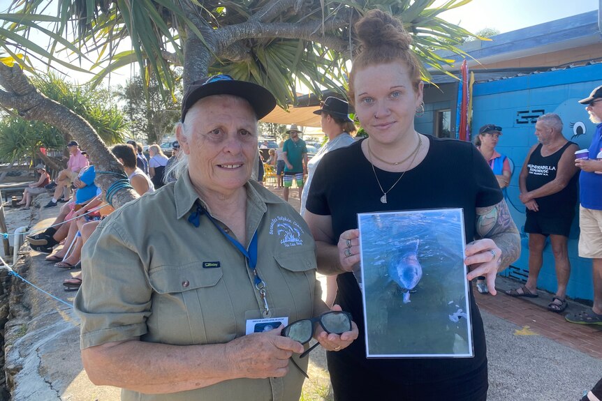Two workers from Barnacles Dolphin centre holding a picture and a pair of sunglasses.